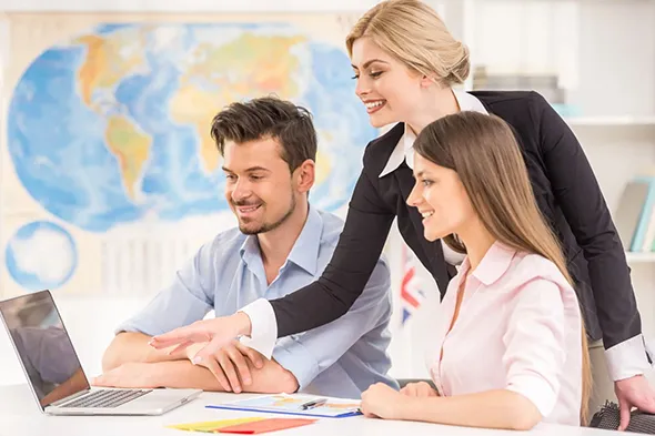 Travel agent in office guiding couple in planning their next vacation on laptop.